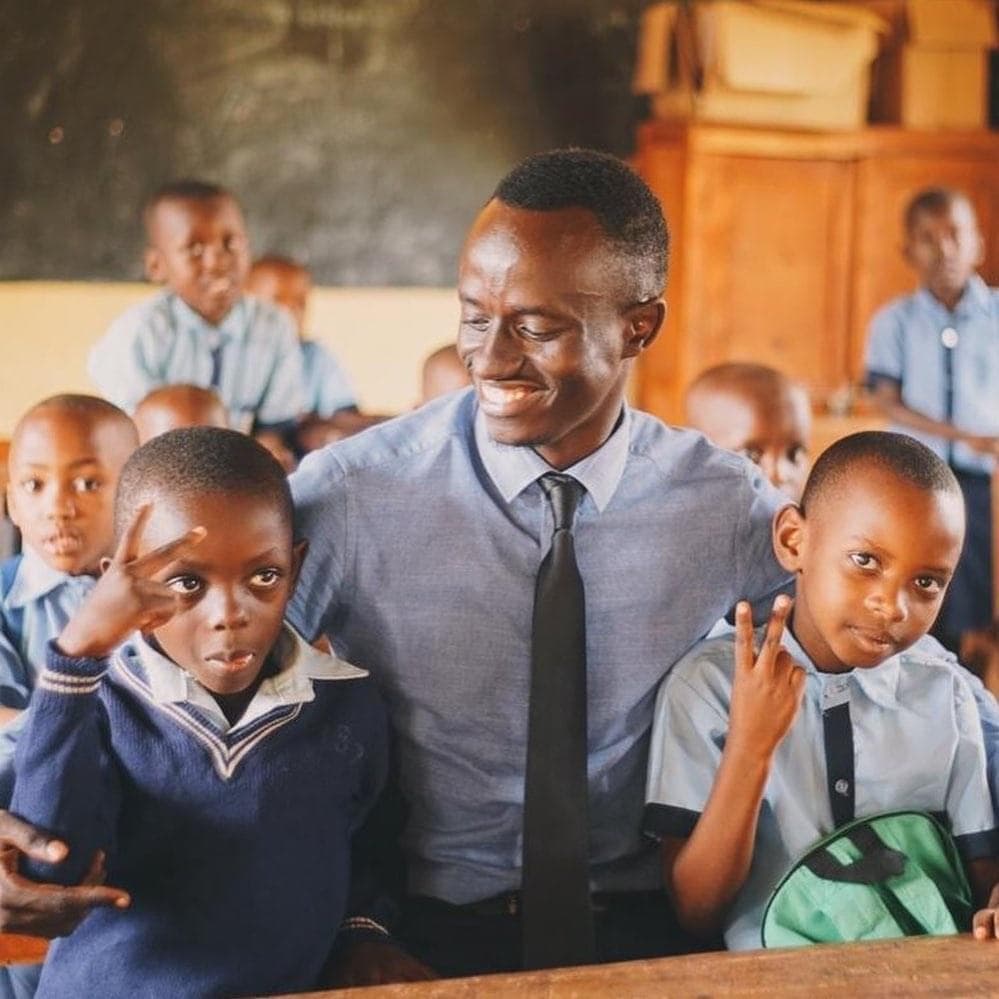 Bertrand Ishimwe smiling with two schoolboys in their classroom