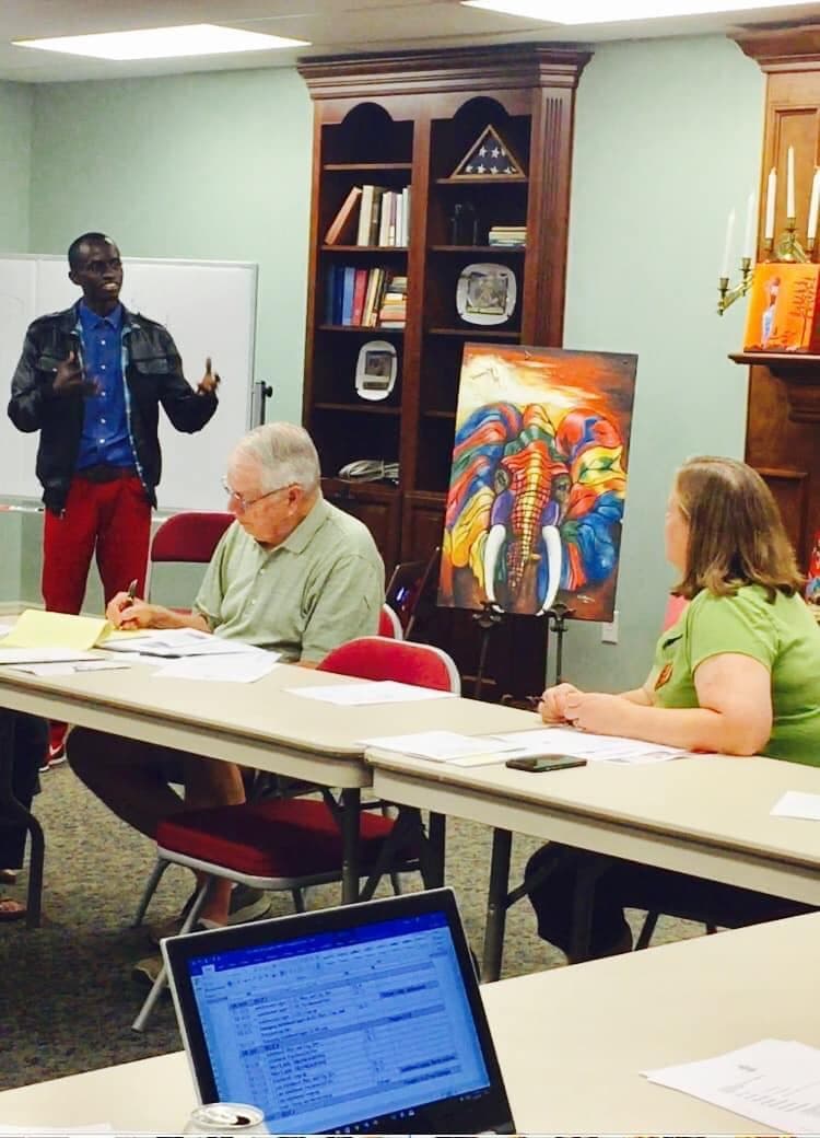 Bertrand Ishimwe speaking beside his elephant painting