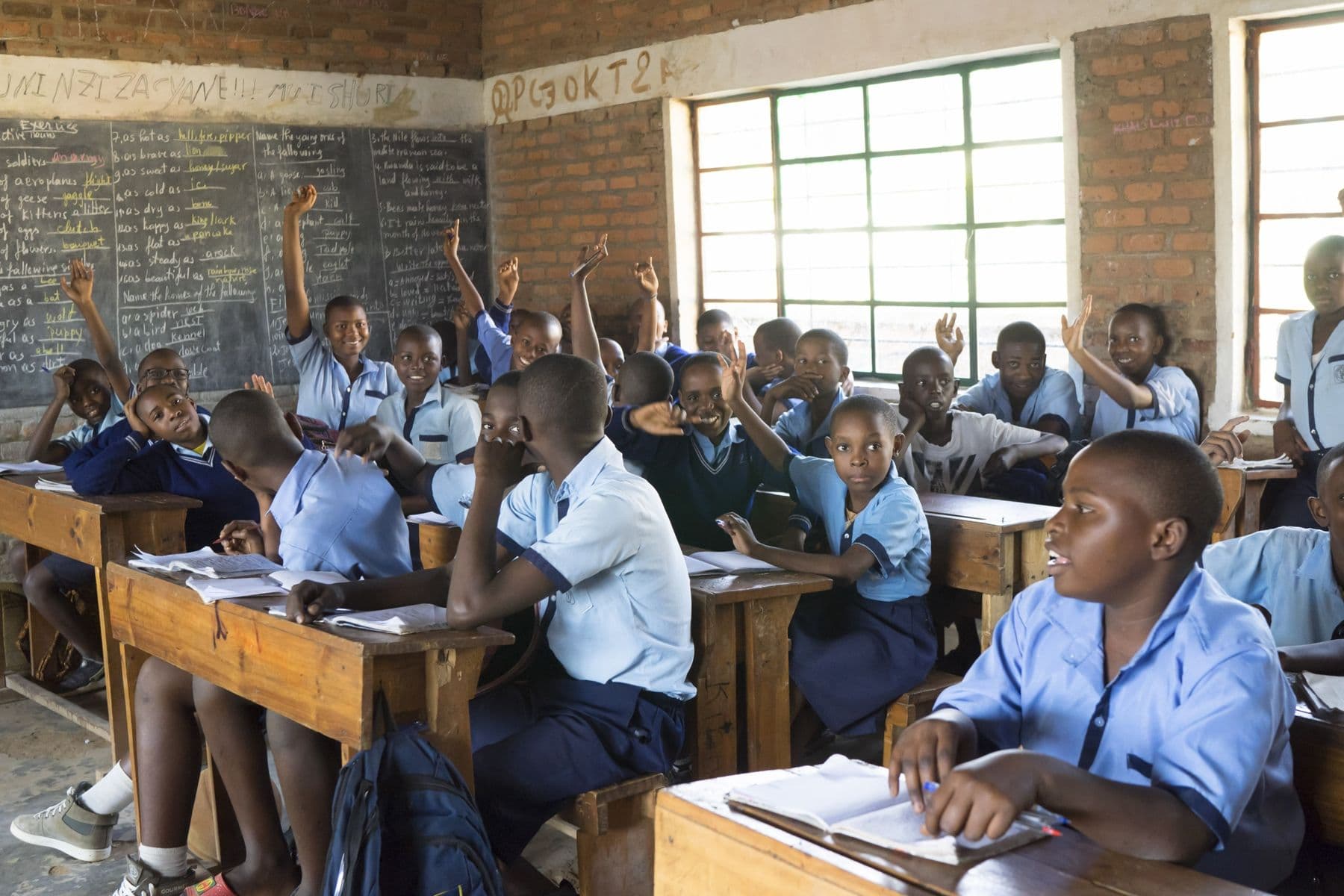 Students in blue school uniforms raising their hands in class