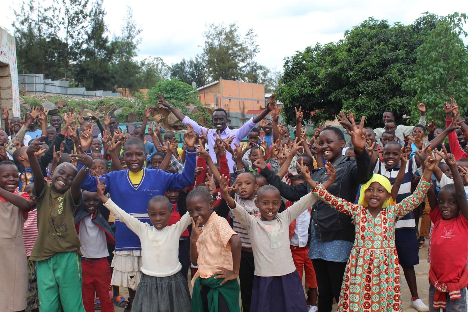 Irembo children and youth gathered together outdoors, arms raised