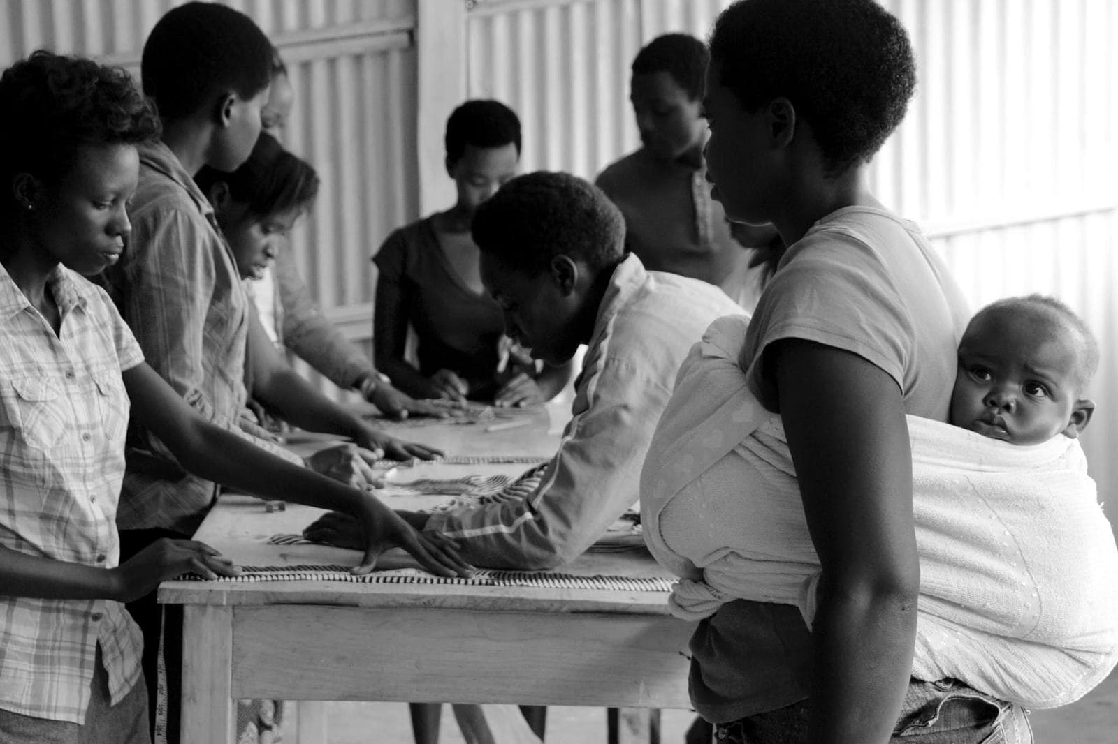 Women measuring fabric together, one carrying her baby on her back