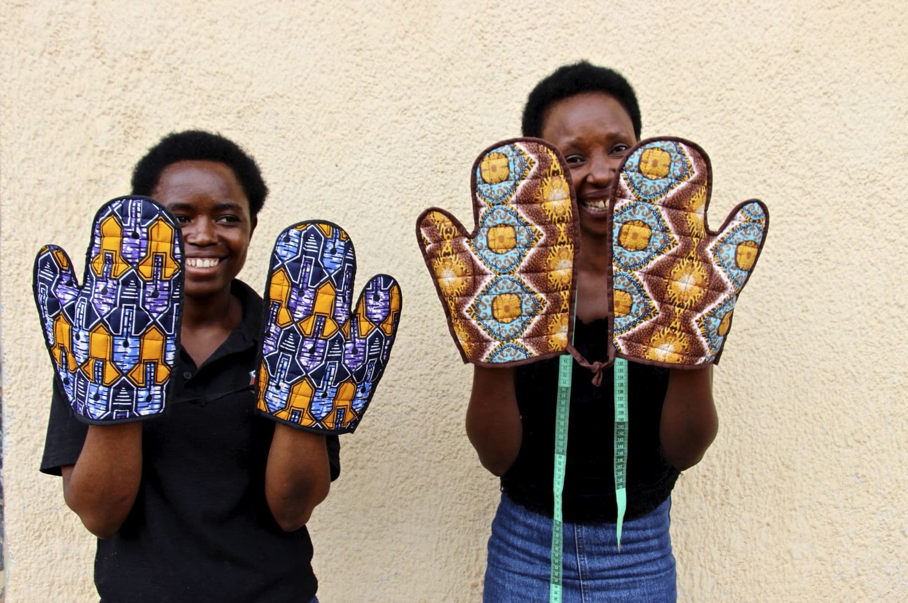 Two Mama Rwanda trainees holding up oven mitts they sewed