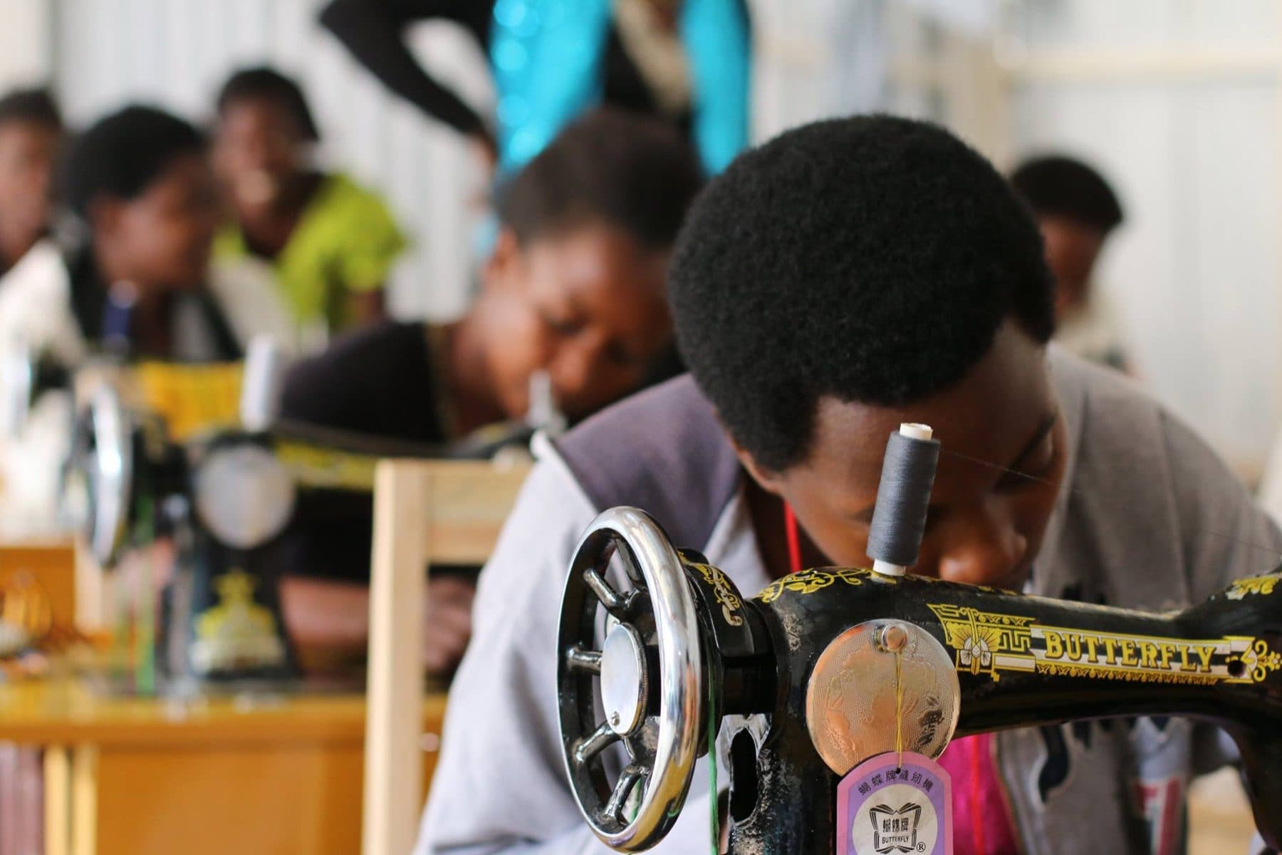 Women learning to sew at a row of sewing machines in the Mama Rwanda training room