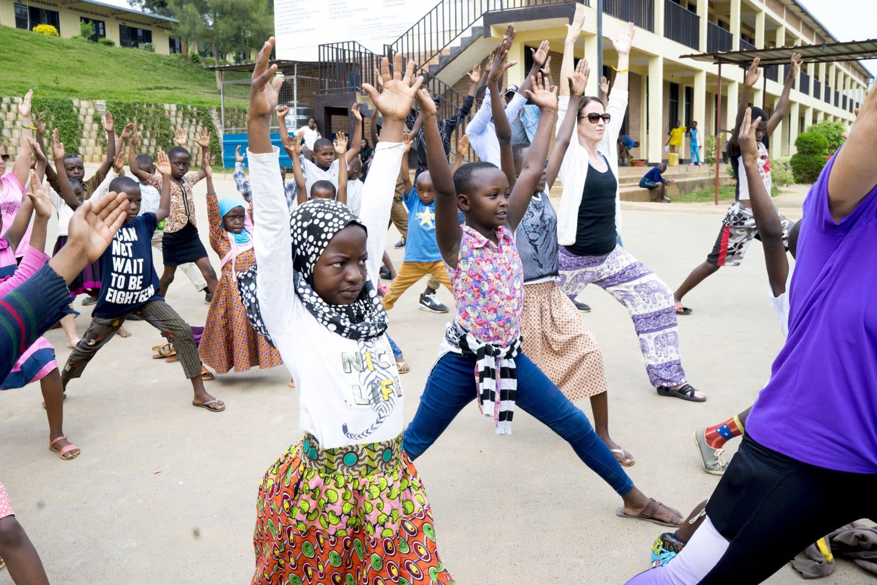 Children and visitors stretching their arms up together in a school courtyard