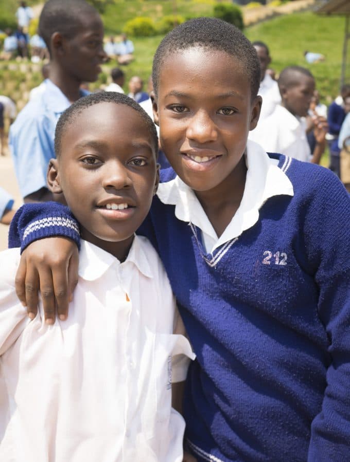 Two schoolboys in uniform smiling with their arms around each other