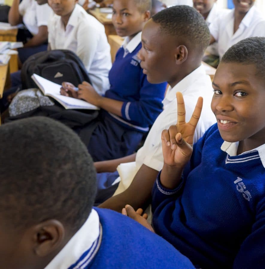 Smiling students in their classroom, one making a peace sign